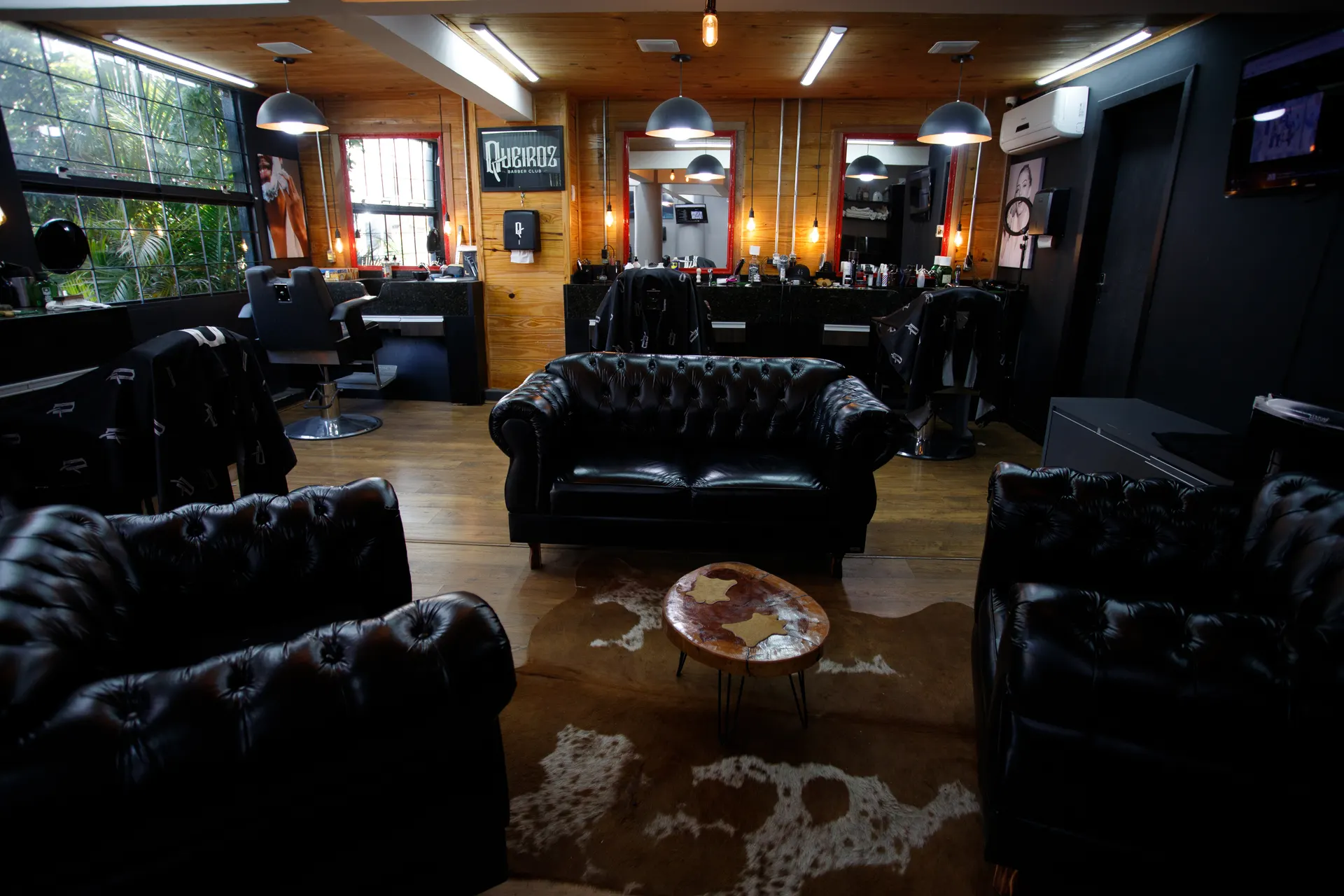 Interior da Queiroz Barber Club em Viamão — sala de espera com sofás de couro e bancadas de atendimento